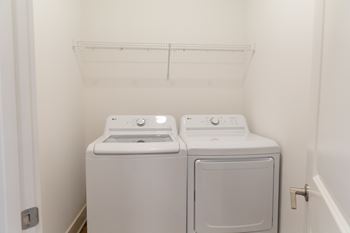 Two white front load washing machines in a small laundry room at The Crest at Oakwood Apartments, Oakwood , Georgia